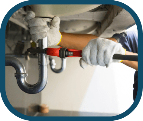 A person wearing white gloves uses a red pipe wrench to tighten or loosen a metal pipe under a sink during a Kitchen Plumbing Repair in Denver. | High 5 Plumbing, Heating & Cooling