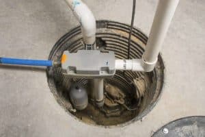 A sump pump system installed in a basement pit includes PVC pipes for discharge, a float switch, electrical wiring, and a corrugated liner set into concrete—ideal for effective water removal and easy regular sump pump maintenance. | High 5 Plumbing, Heating & Cooling