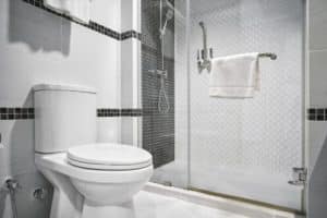 A modern bathroom with a white toilet, glass-enclosed shower, wall-mounted towel rack with a white towel, and stylish black-and-white tile accents showcases how indoor plumbing has evolved since the first people began to invent sanitation systems. | High 5 Plumbing, Heating & Cooling