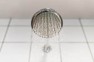 A close-up view of a round showerhead with soft water spraying down, creating a gentle flow that's kind to your hair and skin, against a background of white tiled wall. | High 5 Plumbing, Heating & Cooling