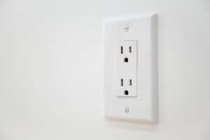 A white electrical outlet with two sockets is mounted on a white wall. The outlet cover, secured with two visible screws, may need electrical outlet troubleshooting if the power outlet is not working but the breaker not tripped. | High 5 Plumbing, Heating & Cooling