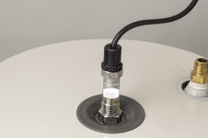 A coaxial cable is connected to a metal socket on a white surface, while another nearby socket—used in water heater anode rod comparison—remains unplugged. Both sockets are mounted on circular metal bases. | High 5 Plumbing, Heating & Cooling